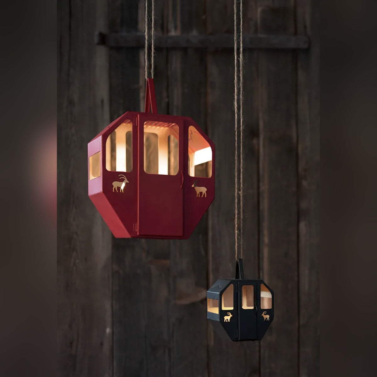 Gondel Laternen in Rot und Schwarz in zwei Größen mit Teelicht beleuchtet, an Seilen vor dunkler Holzwand hängend