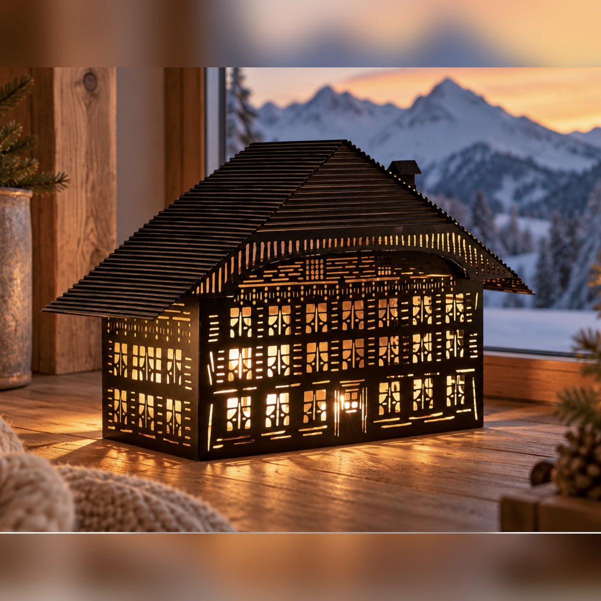 Großes alpines Lichthaus leuchtet am Fenster vor Bergkulisse
